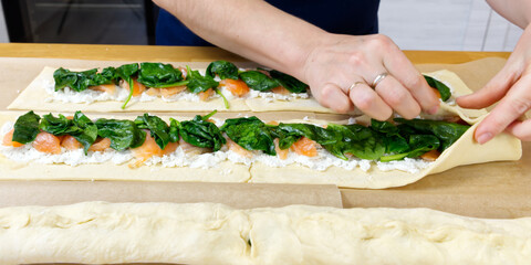 the cook puts spinach and trout on the dough. Savory Christmas pie in the shape of a wreath cooking process. close up