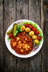 Breaded fried pork chop with fried potatoes and vegetables on wooden table
