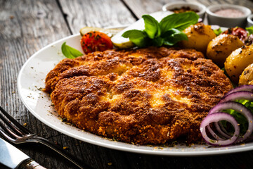 Breaded fried pork chop with fried potatoes and vegetables on wooden table
