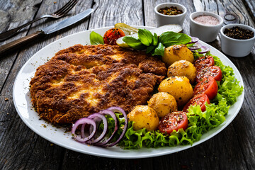 Breaded fried pork chop with fried potatoes and vegetables on wooden table
