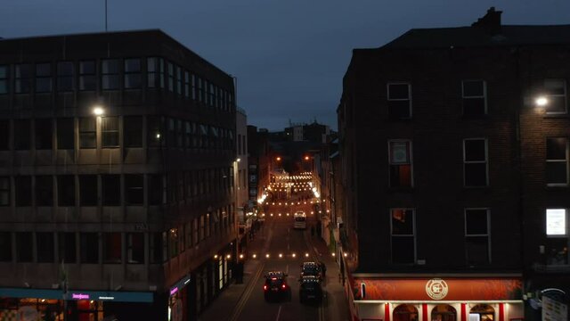 Forwards fly above illuminated narrow street in city centre. Decorative light chains across aisle. Night scene. Limerick, Ireland