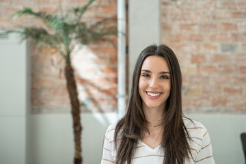 Portrait of young woman creative professional employee in a modern office with brick walls doing...