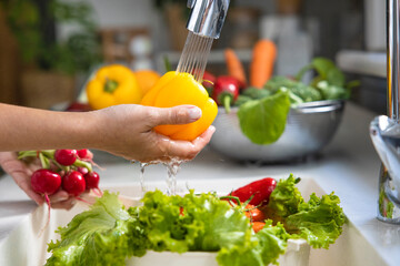 Woman washing vegetables on kitchen counter.