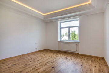 An empty bright room without furniture with a high ceiling and brown laminate. New modern house without furniture