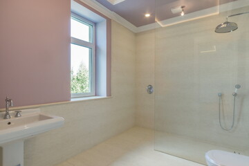 A bright bathroom in pastel colors with a window and a glass shower partition.