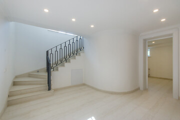 Cozy bright hall with soft outlines of the walls, beige laminate. Stairs with handrails and an entrance door.