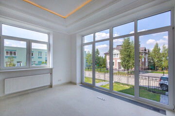 An empty, bright, unfurnished living room with a high ceiling and a panoramic window. New modern house without furniture