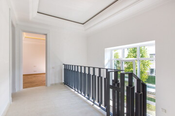 A bright hall with a high ceiling, blue staircase railings and an entrance to the living room. New modern house without furniture