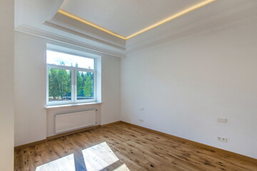 An empty bright room with a high ceiling without furniture and a brown laminate floor.