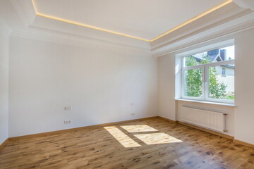 A bright room without furniture, with a high ceiling, a window and brown laminate flooring.