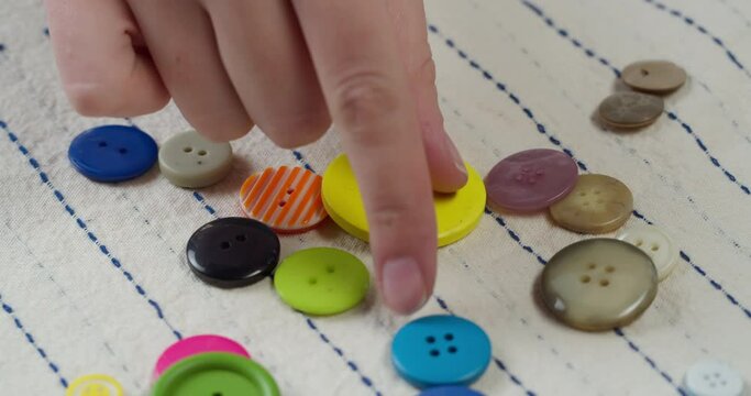 Colorful buttons falling on striped fabric close-up. Tailoring clothes and professional sewing concept. Choosing button accessories for material.