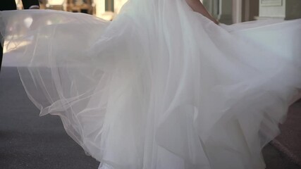 The bride in a long white wedding dress is whirling about, blowing a gown in the wind. A loving couple of newlyweds is walks in the city. Summer romance, man and woman. - Powered by Adobe