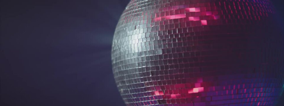 Cropped shot of rotating silver disco ball reflecting colourful light. Night party in club, music and entertainment concept.