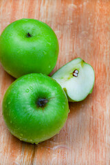 fresh and crisp green granny smith apples on wooden surface with water droplets
