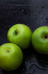 fresh and crisp green granny smith apples on black surface with water droplets