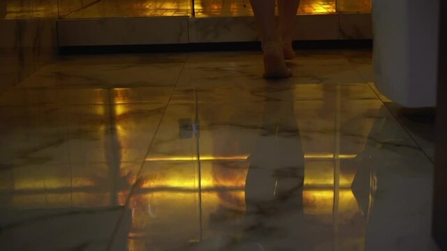 A young woman walks barefoot on the marble tiles on the bathroom floor. Morning girls, legs.