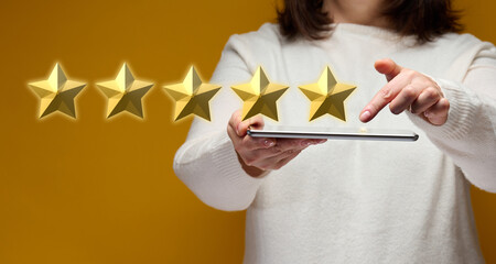 female hand holding an electronic gadget tablet on a yellow background, five gold stars