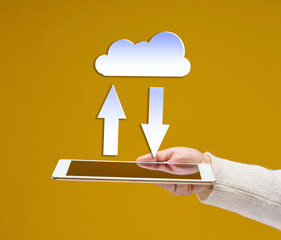 female hand holds an electronic gadget tablet on a yellow background, white cloud with arrows above...