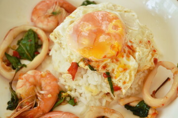 spicy stir fried shrimp and squid basil leaf topping egg eat couple with rice on plate