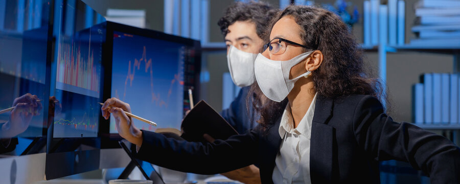 team brokers wearing face mask look at stock market graph on monitor computer to analyze before offer and arranges transactions between buyer and seller for a commission when the deal is executed