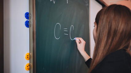 The girl is writing a chemical formula on the blackboard in the classroom.
