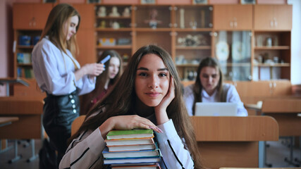 A student poses with textbooks at her desk in her class.