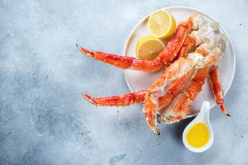 White plate with kamchatka crab claws, lemon and butter. Top view on a light-blue stone background,...