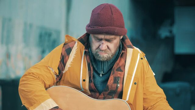 A poor man is playing the guitar in the street
