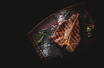 Grilled T-bone Steak on bones on wooden plate on bkack background