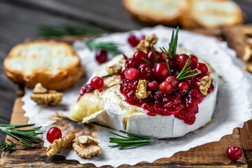 Delicious hot baked camembert with fresh rosemary, cranberry sauce and baguette bread on wooden table. banner, catering menu recipe place for text, top view - Powered by Adobe