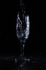 Clean wineglass with splashes made by pouring water on black background in studio 