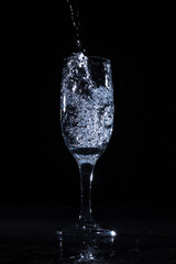 Clean water pouring in clear goblet making splashes in studio on black background
