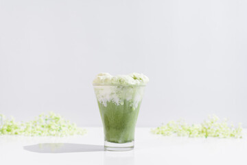 Un vaso de té matcha con leche decorado con flores   sobre una mesa blanca