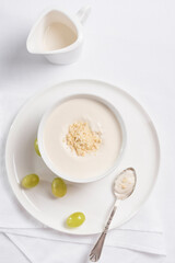 Crema de almendras, sopa fría española. Ajo blanco de Málaga con almendras y uvas en un recipiente blanco sobre una mesa blanca. Vista superior