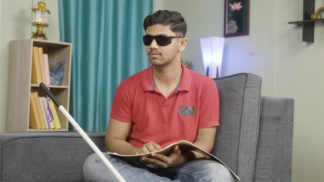 Disabled blind young man reading by touching book at home - concept of education, self development and learning