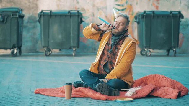 A beggar in a birthday hat is sitting on the ground and cheering