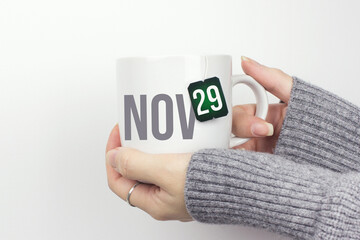 November 29th. Day 29 of month, Calendar date. Closeup of female hands in grey sweater holding cup of tea with month and calendar date on teabag label. Autumn month, day of the year concept.