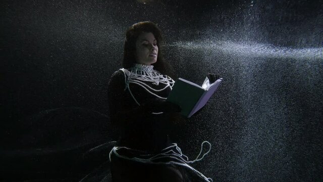 elegant brunette lady is reading old book underwater, subaquatic shot, magic and fairytale