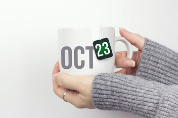 October 23rd. Day 23 of month, Calendar date. Closeup of female hands in grey sweater holding cup of tea with month and calendar date on teabag label. Autumn month, day of the year concept.