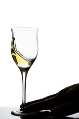 Backlit hand of a man moving a glass of white wine. White background. Concept of movement, elegance, taste.