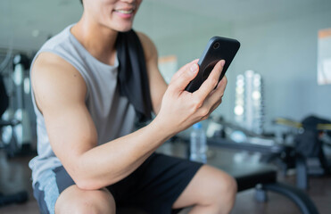 Fototapeta na wymiar close up young asian man use smartphone to check news on social media or chat with friends using rest after workout in gym for health and modern lifestyle concept