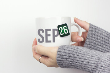 September 26th. Day 26 of month, Calendar date. Closeup of female hands in grey sweater holding cup of tea with month and calendar date on teabag label. Autumn month, day of the year concept.