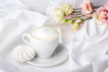 Obraz na płótnie Canvas Refreshing morning scene featuring a creamy cup of cappuccino, paired with a delicate meringue, set amidst gentle floral hues on a silken sheet.