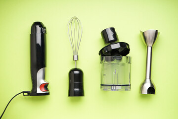 Black plastic electrical hand blender with stainless steel body and accessory on the green background, top view.