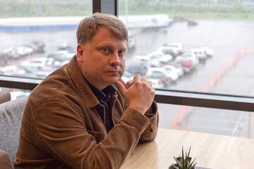 Portrait of an adult man in a corduroy jacket waiting for his order at a table in a cafe.