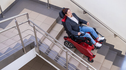 Fototapeta premium Caucasian woman in electric caterpillar wheelchair climbs up stairs.