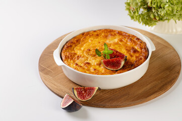 curd casserole with pumpkin in a round white shape on a wooden board, light table, decorated with figs, restaurant serving