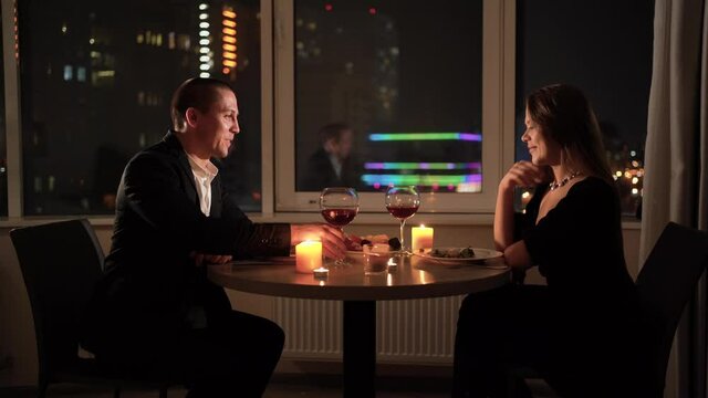 romantic dinner at home for two. A couple in love sits at a table, a man says a toast and raises a glass. concept for celebrating valentine's day or anniversary. Red wine and candles on the table.