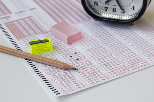 Alarm clock,wooden pencil and rubber on filled exam sheet,conceptual image of education qualifying test exam.