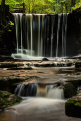 Epic beautiful Autumn landscape image of Nant Mill waterfall in Wales with glowing sunlight through the woodland